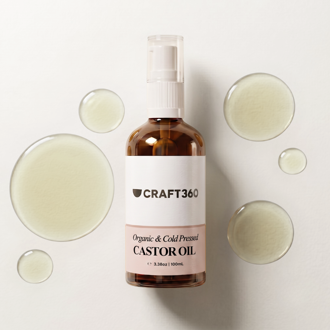 A bottle of Craft 360 Organic & Cold Pressed Castor Oil centered on a white background, surrounded by decorative translucent droplets. The bottle is amber glass with a white pump and a white label.